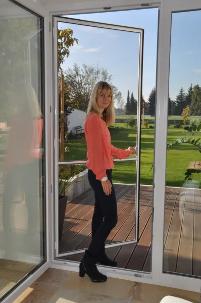 Huber Franz - Insektenschutz - Fenster - Türen – eine Frau öffnet eine Insektenschutztür zum Garten