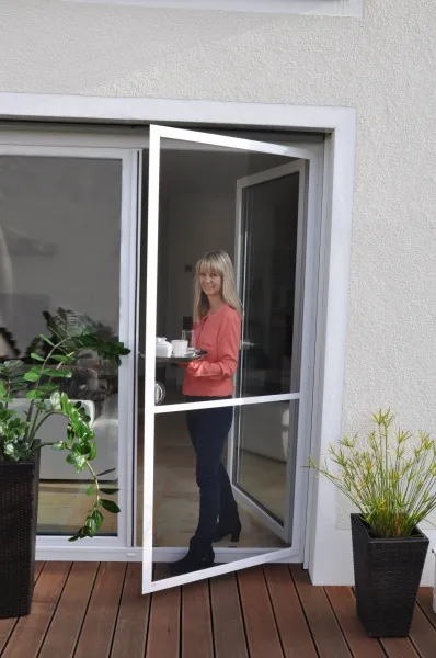 Huber Franz - Insektenschutz - Fenster - Türen – eine Frau öffnet lächelnd ihre Gartentür mit Insektenschutzgitter